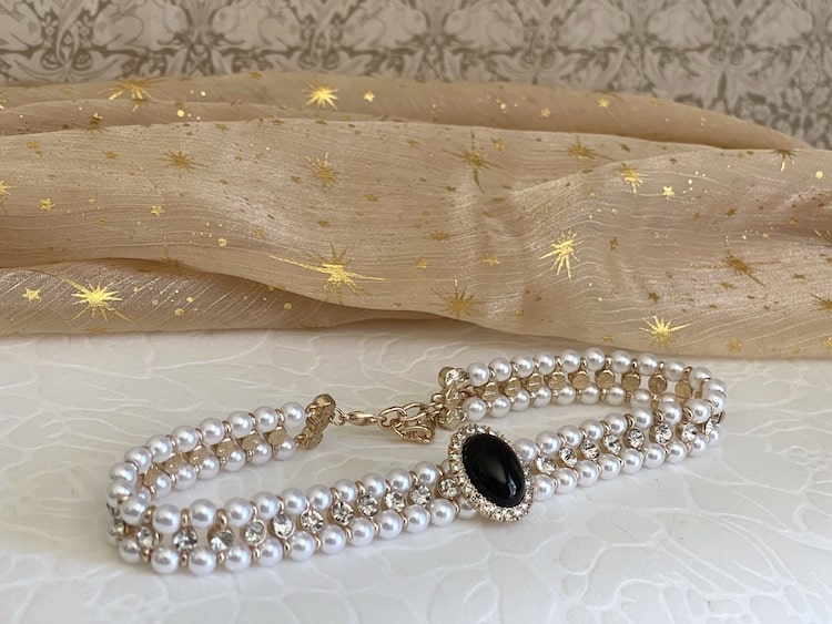 A Historically inspired renaissance tudor baroque rococo regency victorian edwardian pearl beaded crystal accent choker necklace in black is pictured on a floral puff.