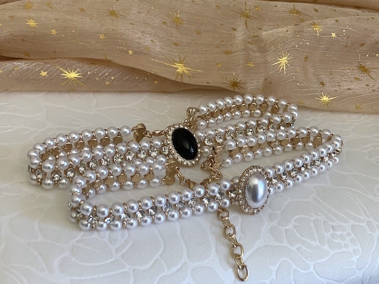 Two Historically inspired renaissance baroque tudor rococo regency victorian edwardian style pearl and crystal choker necklaces are pictured on a floral puff. One black, one white. and gold