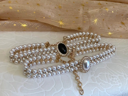 Two historically inspired renaissance tudor baroque rococo regency victorian edwardian pearl beaded crystal accent choker necklaces are pictured on a floral puff. One white, and one black and gold.