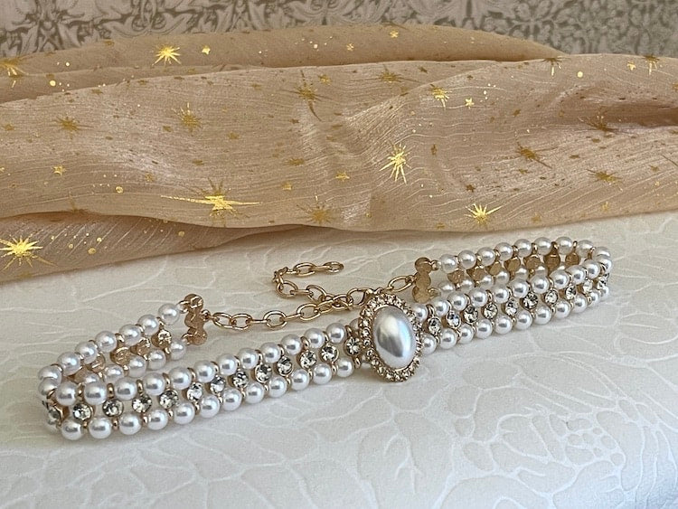 A Historically inspired renaissance baroque tudor rococo regency victorian edwardian style pearl and crystal choker necklace is pictured on a floral puff.