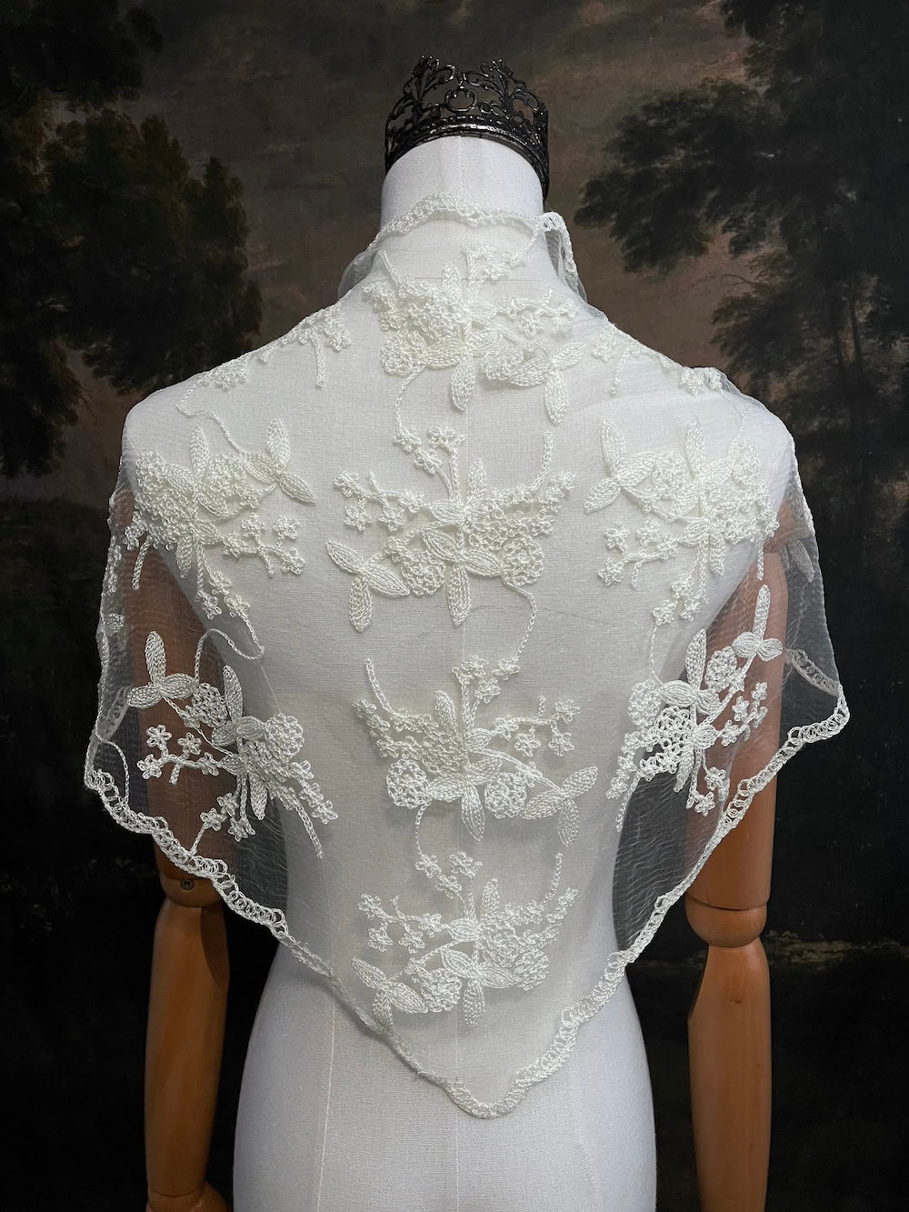 Mannequin wearing a vintage style ivory lace headscarf babushka triangle headdress made from floral embroidery lace as a shawl against an art history background