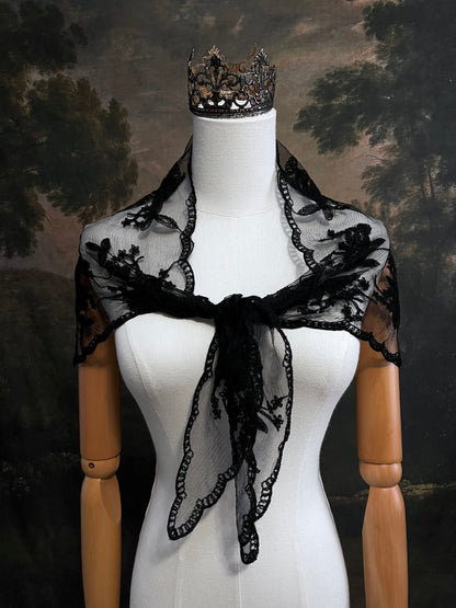 Mannequin wearing a vintage style gothic black lace headscarf babushka triangle headdress made from floral embroidery lace worn as a shawl against an art history background