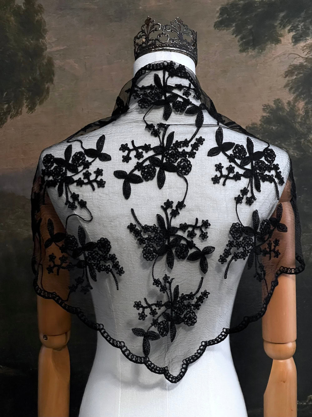 Mannequin wearing a vintage style gothic black lace headscarf babushka triangle headdress made from floral embroidery lace worn as a shawl against an art history background