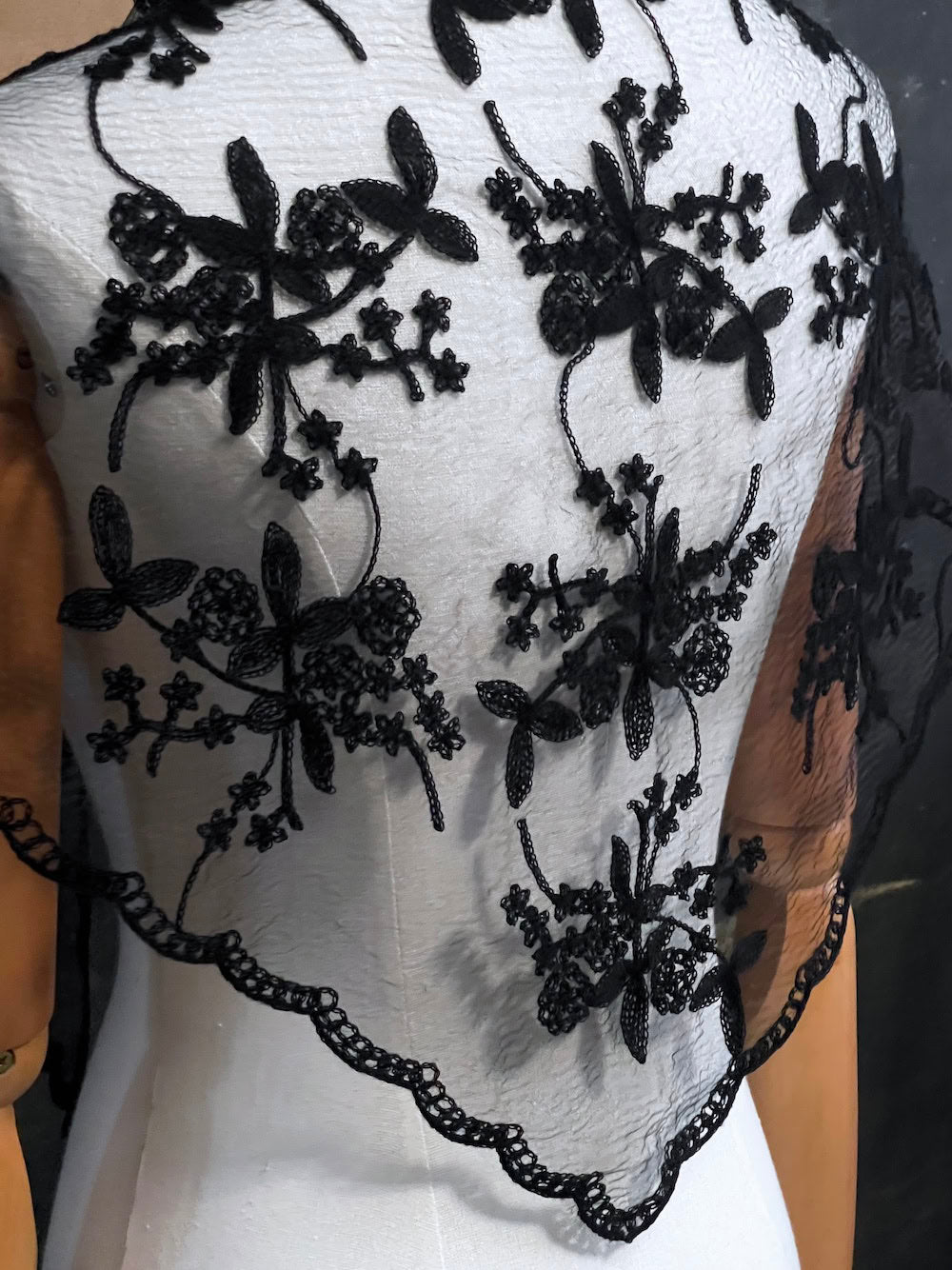 Mannequin wearing a vintage style gothic black lace headscarf babushka triangle headdress made from floral embroidery lace worn as a shawl against an art history background