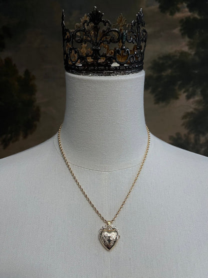 Mannequin wearing a gold twisted chain with a heart shaped locket pendant carved with historically inspired floral filigree