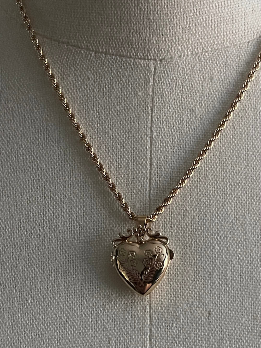 Mannequin wearing a gold twisted chain with a heart shaped locket pendant carved with historically inspired floral filigree