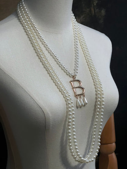 Mannequin wearing a Tudor inspired Anne Boleyn pearl necklace with a decorative 'B' pendant against a dark art history background