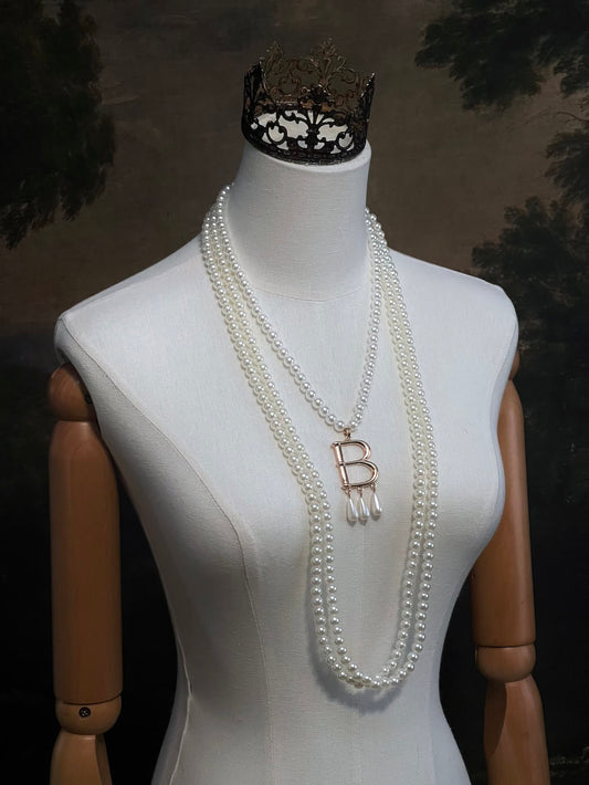 Mannequin wearing a Tudor inspired Anne Boleyn pearl necklace with a decorative 'B' pendant against a dark art history background