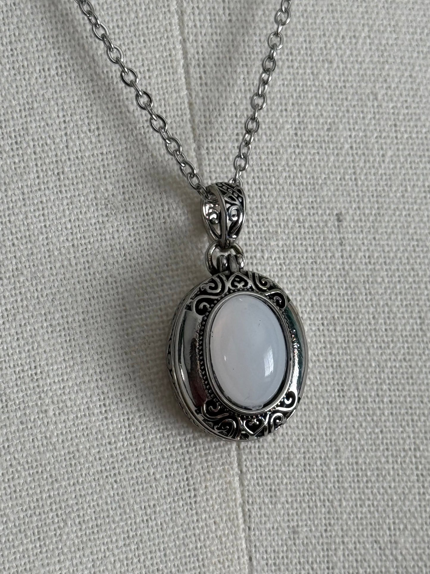 A victorian inspired silverwork locket necklace with filigree designs and a faux moonstone cabochon, pictured on a mannequin