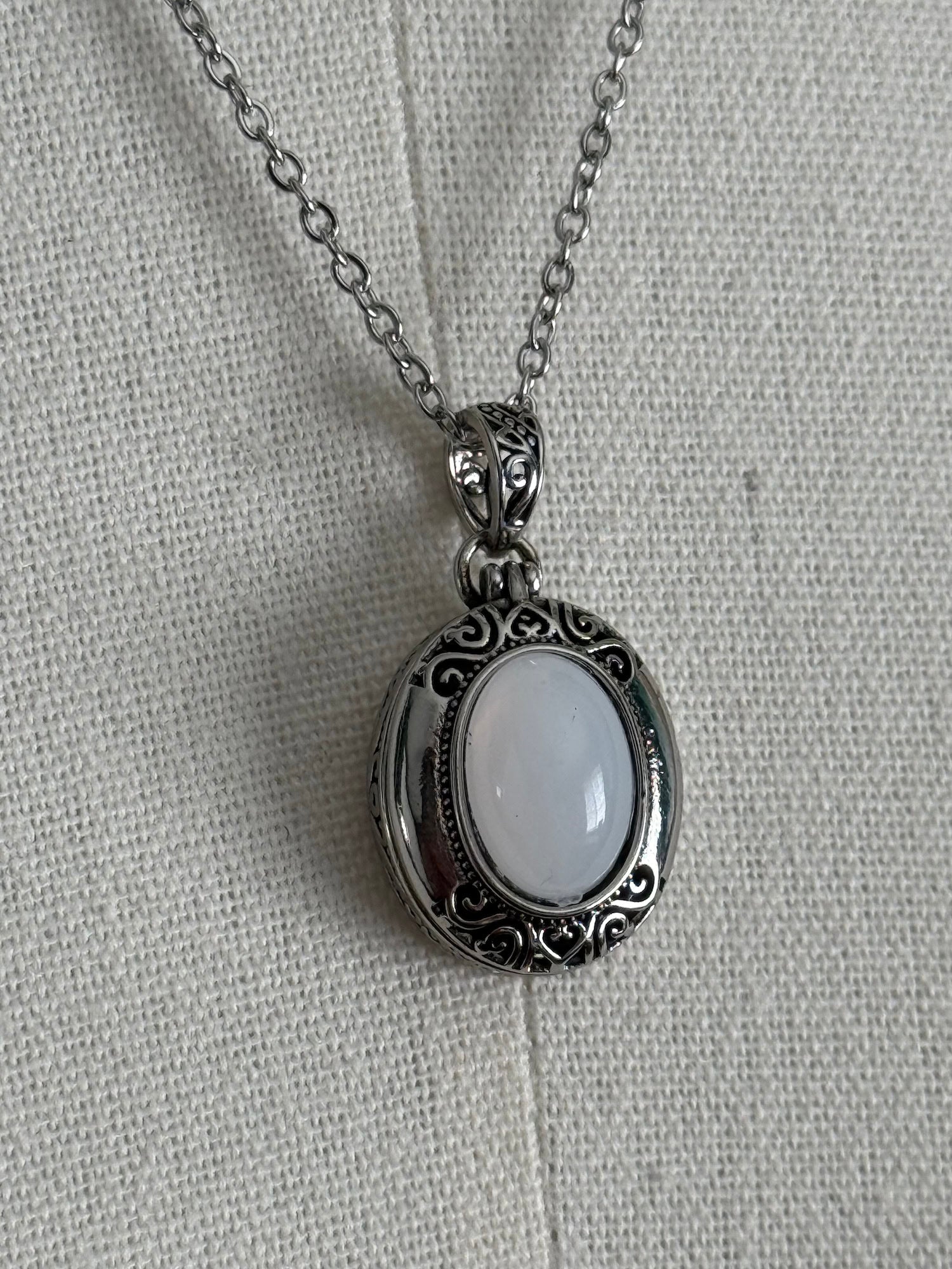 A victorian inspired silverwork locket necklace with filigree designs and a faux moonstone cabochon, pictured on a mannequin