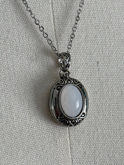 A victorian inspired silverwork locket necklace with filigree designs and a faux moonstone cabochon, pictured on a mannequin
