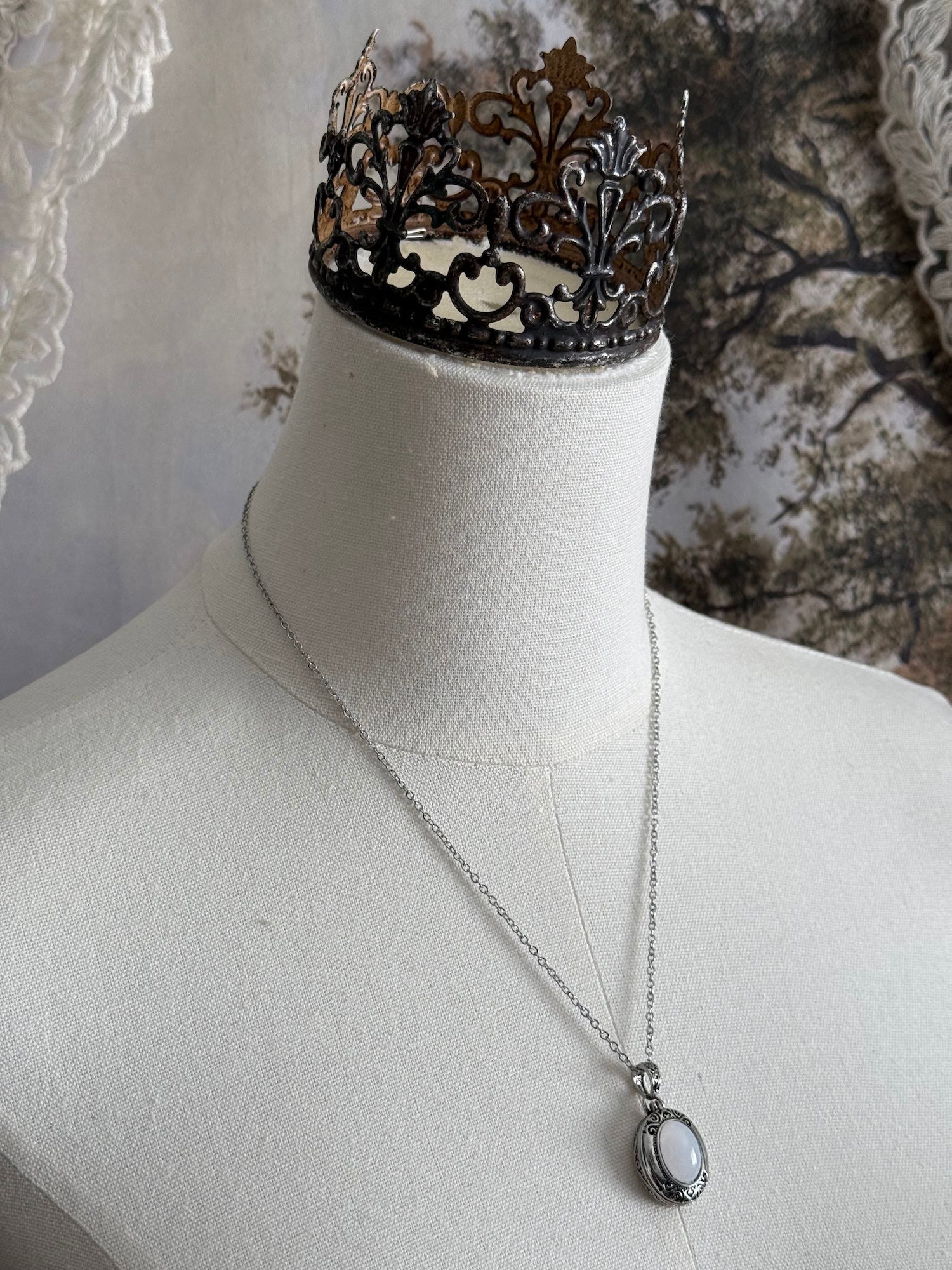 A victorian inspired silverwork locket necklace with filigree designs and a faux moonstone cabochon, pictured on a mannequin