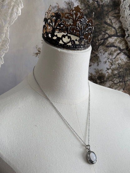 A victorian inspired silverwork locket necklace with filigree designs and a faux moonstone cabochon, pictured on a mannequin