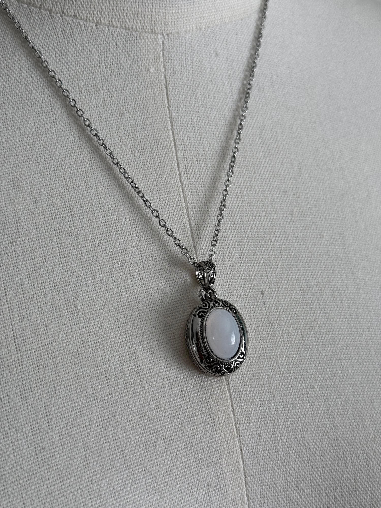 A victorian inspired silverwork locket necklace with filigree designs and a faux moonstone cabochon, pictured on a mannequin