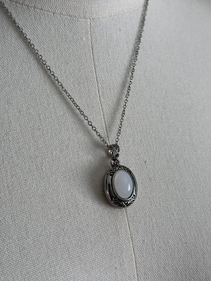 A victorian inspired silverwork locket necklace with filigree designs and a faux moonstone cabochon, pictured on a mannequin