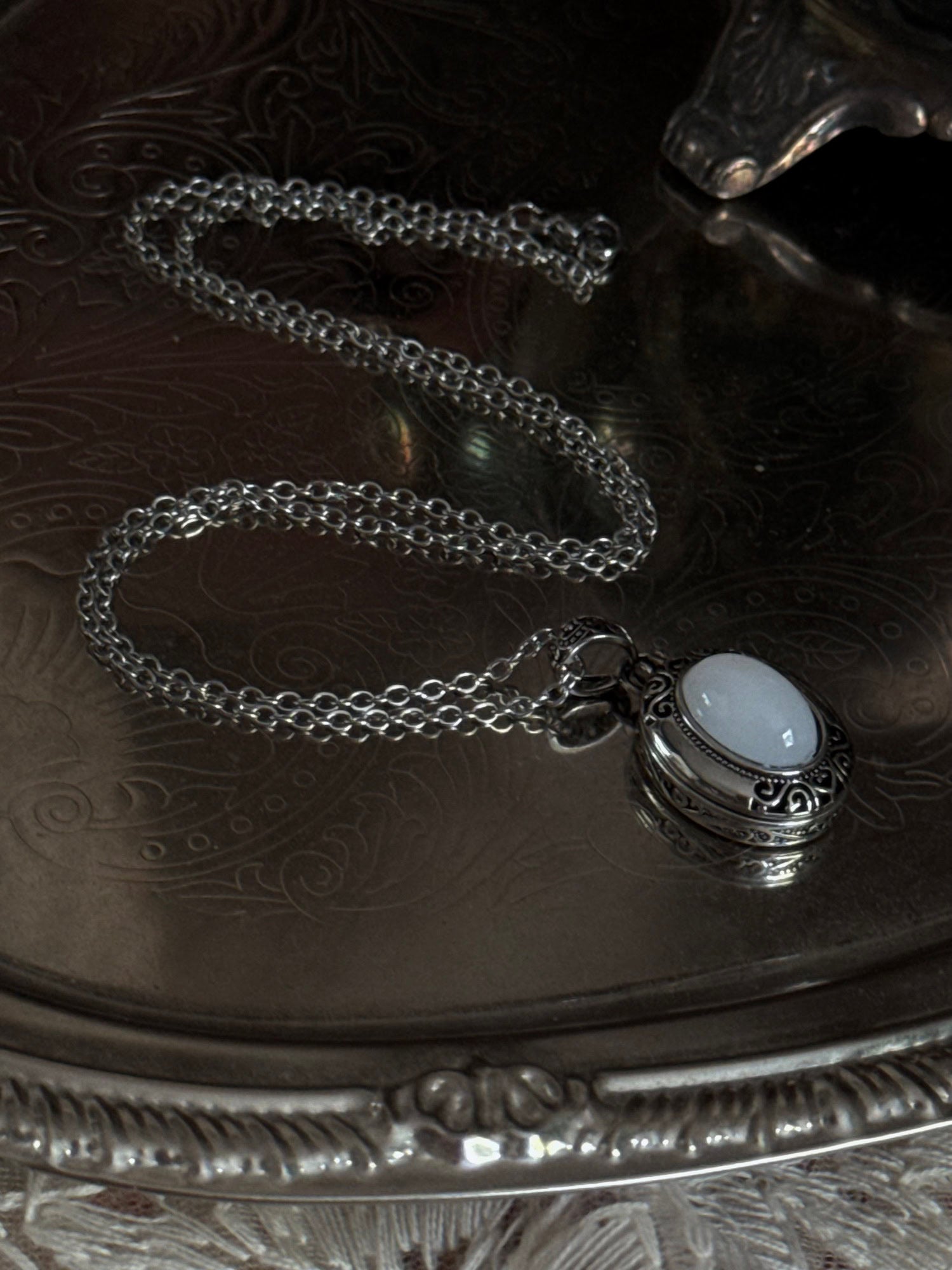 A victorian inspired silverwork locket necklace with filigree designs and a faux moonstone cabochon, pictured on a mannequin