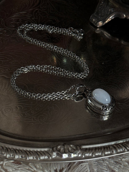 A victorian inspired silverwork locket necklace with filigree designs and a faux moonstone cabochon, pictured on a mannequin