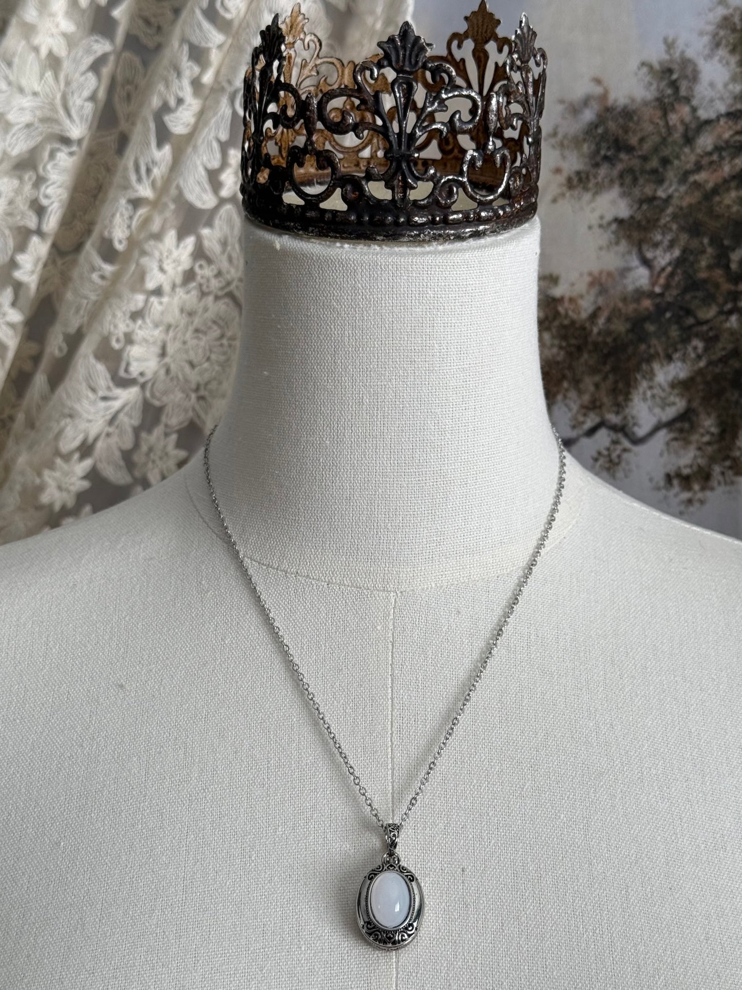 A victorian inspired silverwork locket necklace with filigree designs and a faux moonstone cabochon, pictured on a mannequin