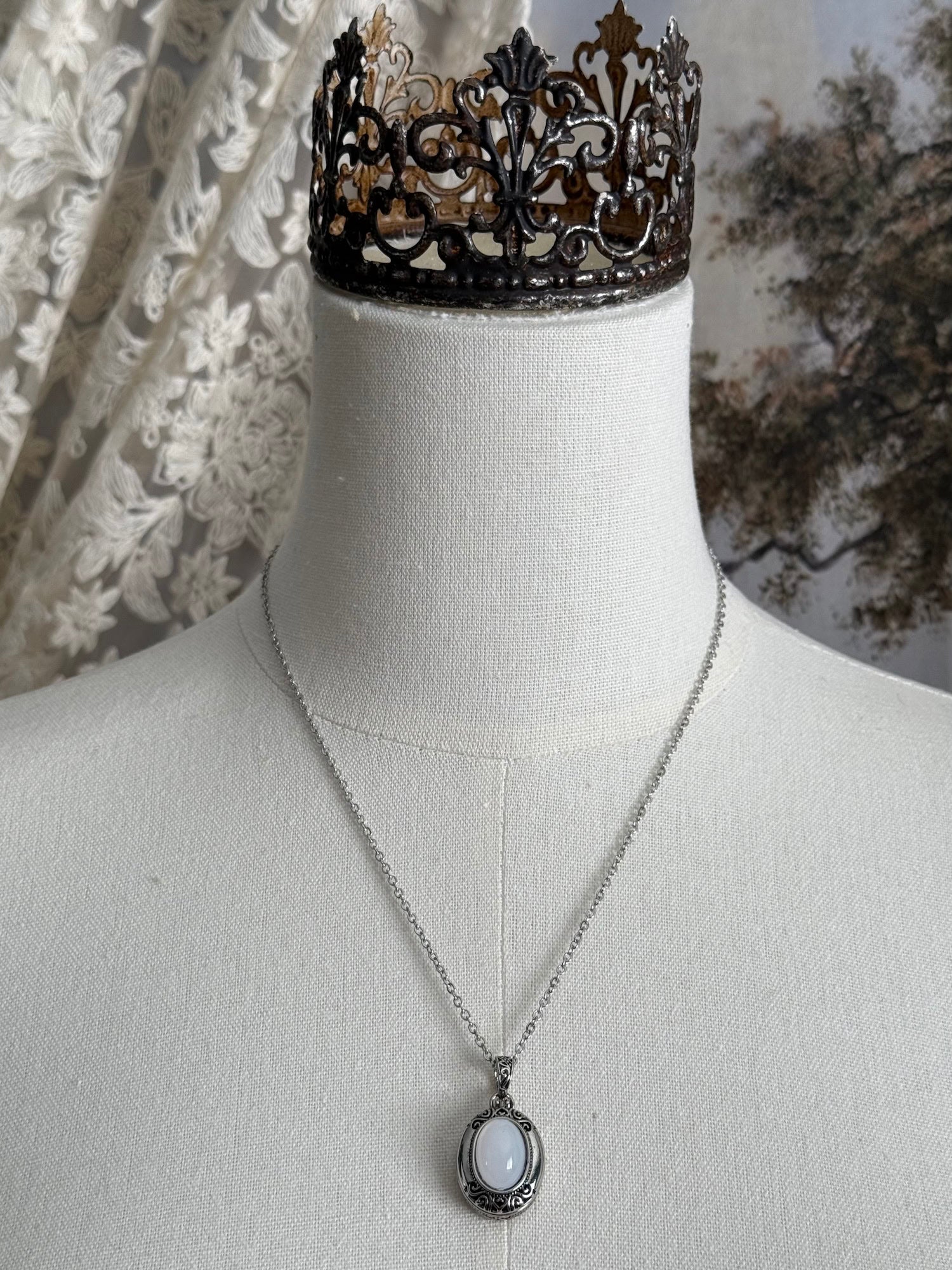 A victorian inspired silverwork locket necklace with filigree designs and a faux moonstone cabochon, pictured on a mannequin