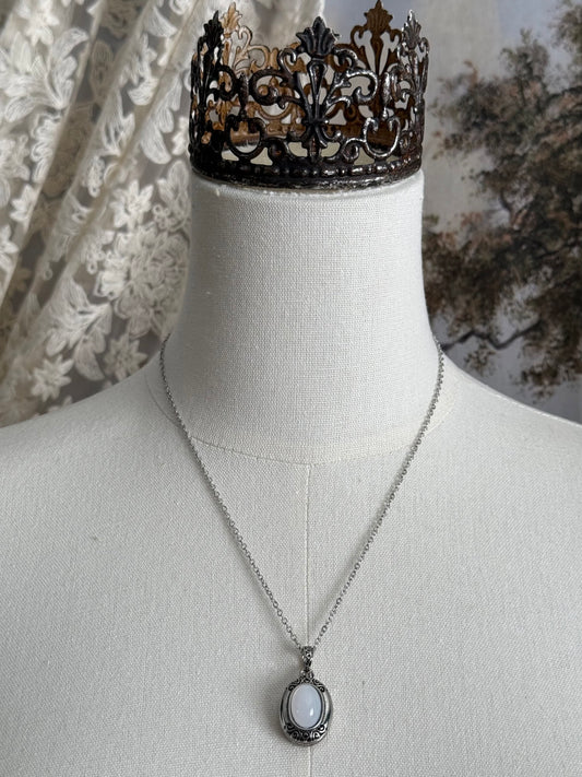 A victorian inspired silverwork locket necklace with filigree designs and a faux moonstone cabochon, pictured on a mannequin