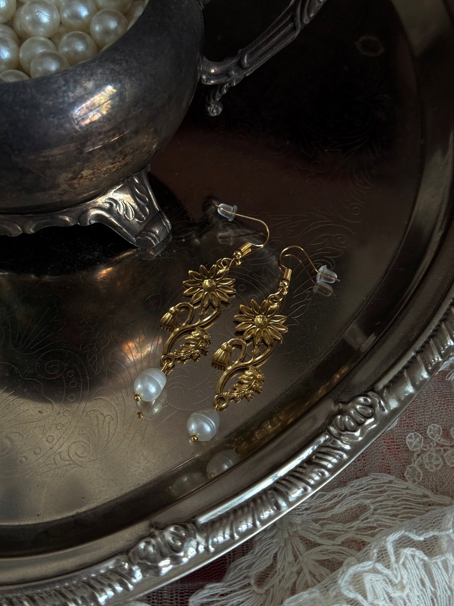 Historically inspired gold toned medieval wildflower daisy earrings with pearl dangle drops, displayed on an antique silver dish.