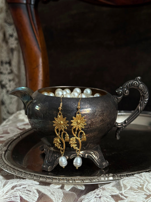 Historically inspired gold toned medieval wildflower daisy earrings with pearl dangle drops, displayed on an antique silver dish.