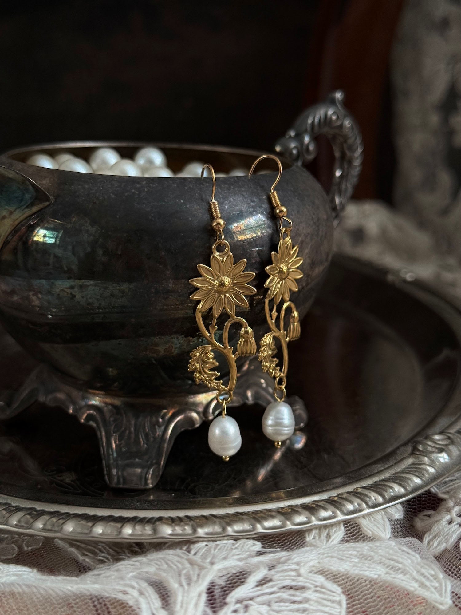 Historically inspired gold toned medieval wildflower daisy earrings with pearl dangle drops, displayed on an antique silver dish.