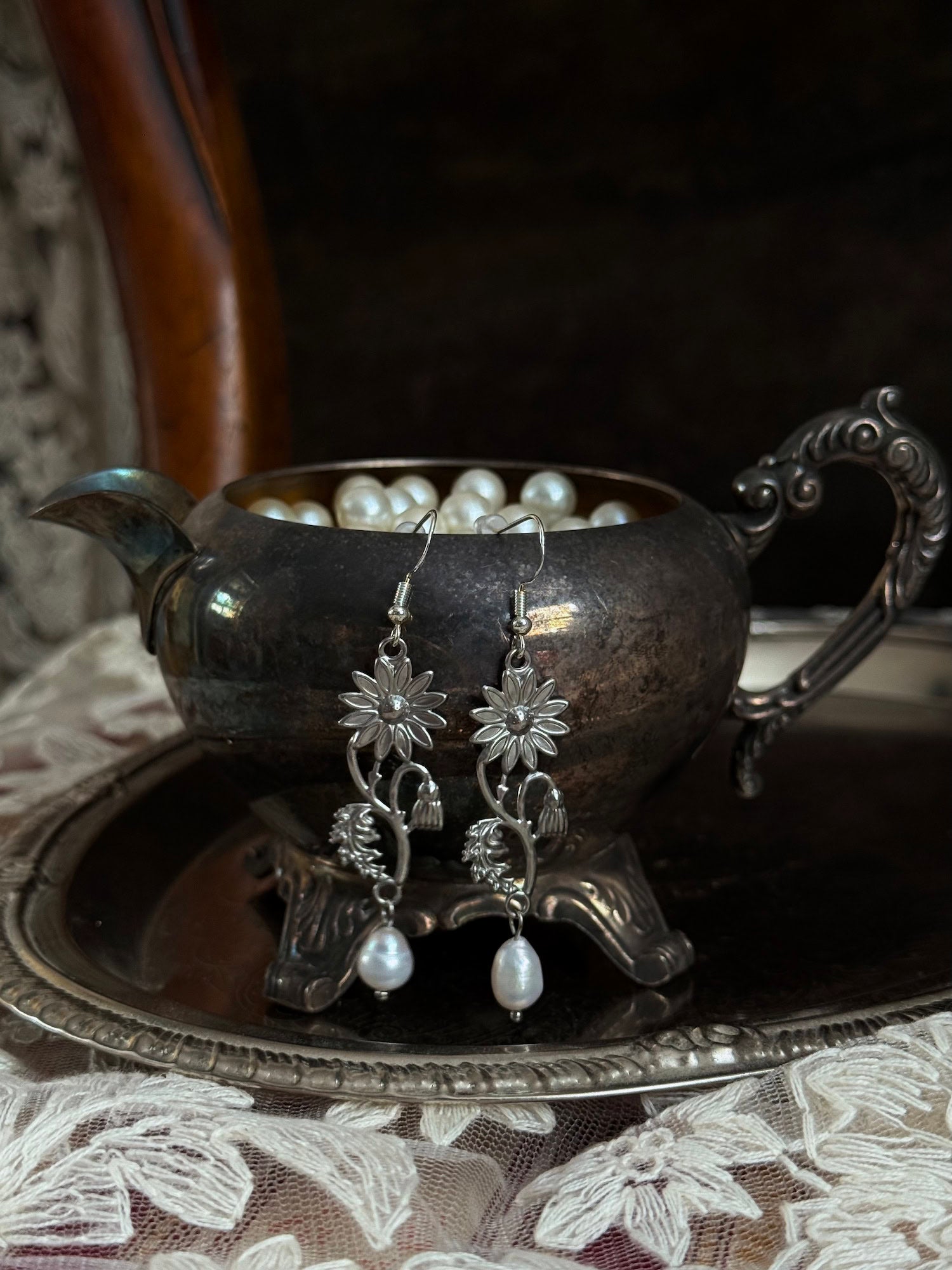 A pair of silver metal medieval wildflower daisy earrings with pearl drop dangles, hanging displayed on an antique silver dish.