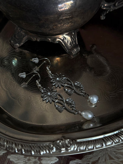 A pair of silver metal medieval wildflower daisy earrings with pearl drop dangles, displayed on an antique silver dish.