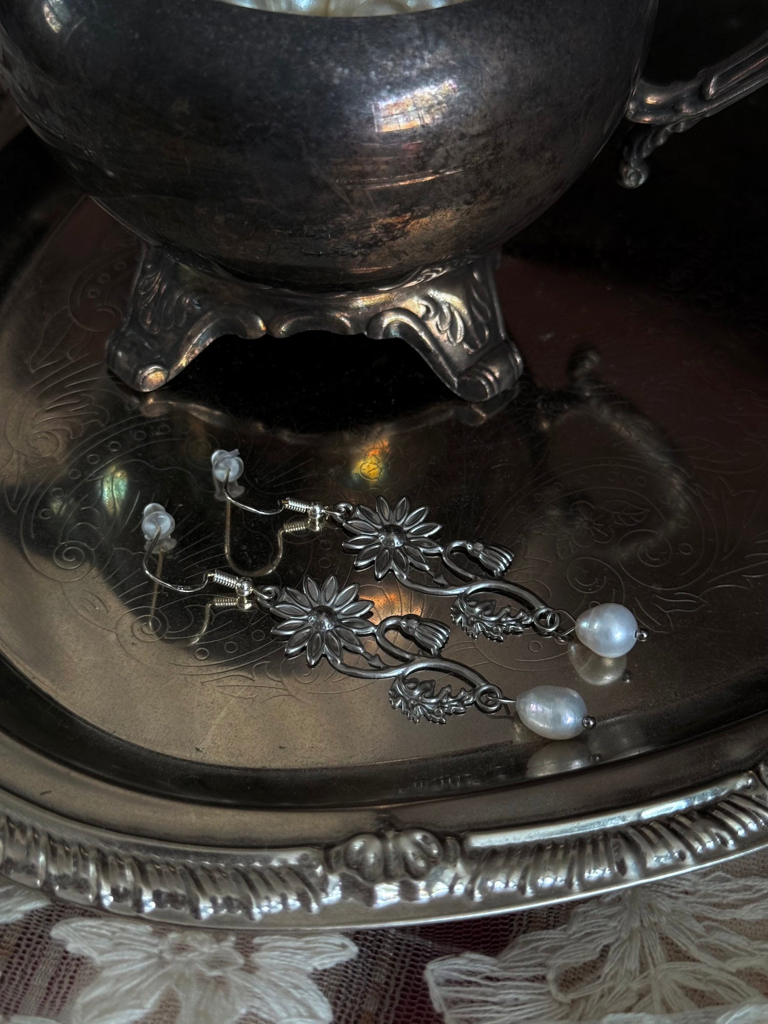 A pair of silver metal medieval wildflower daisy earrings with pearl drop dangles, displayed on an antique silver dish.