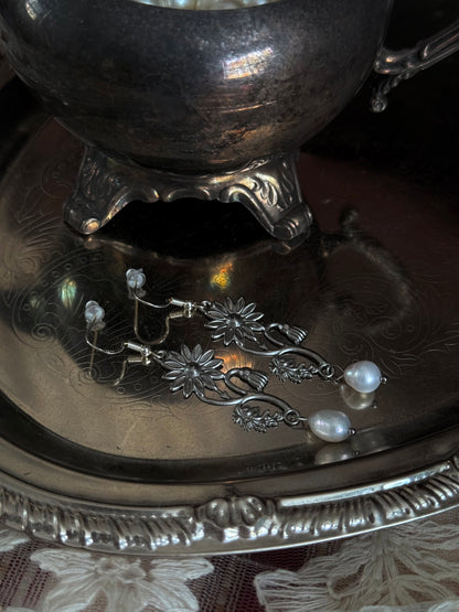 A pair of silver metal medieval wildflower daisy earrings with pearl drop dangles, displayed on an antique silver dish.