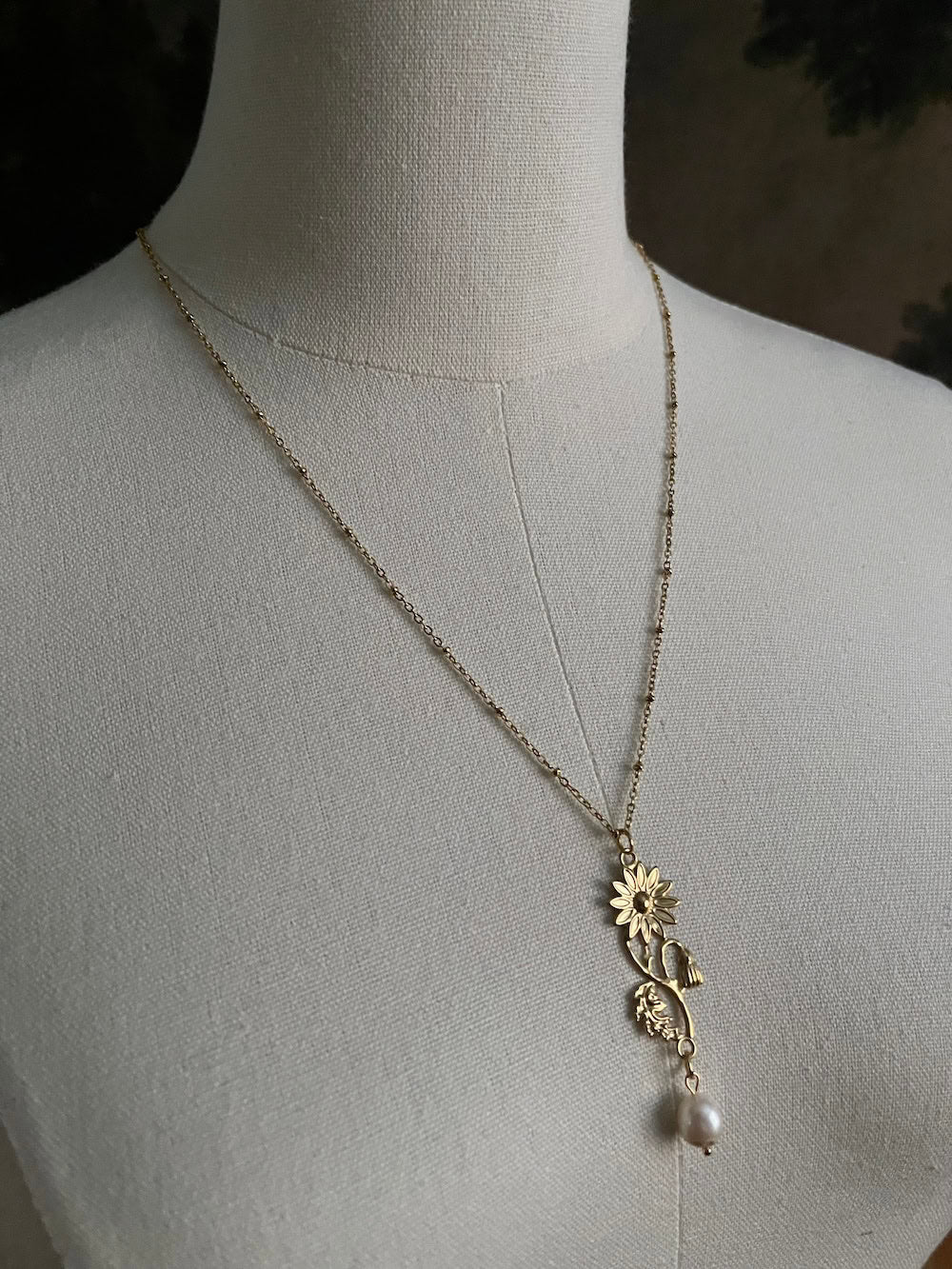 A historical jewelry inspired vintage style daisy flower pendant necklace with pearl dangle in gold toned stainless steel