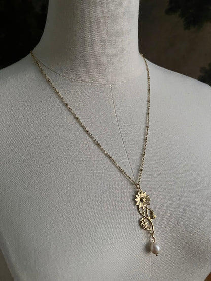 A historical jewelry inspired vintage style daisy flower pendant necklace with pearl dangle in gold toned stainless steel