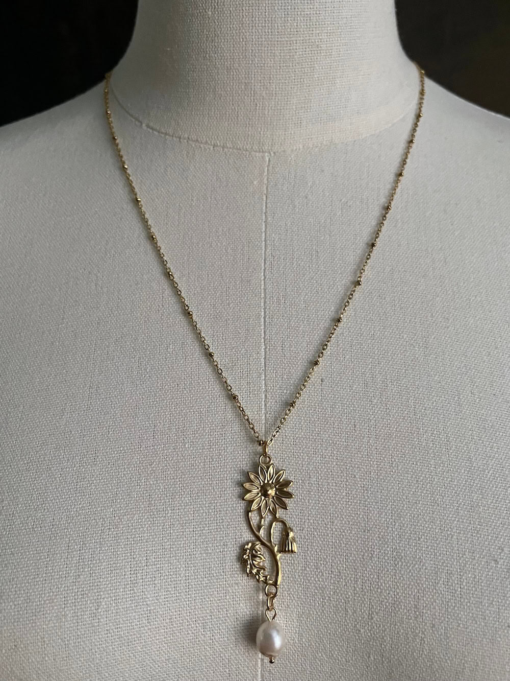 A historical jewelry inspired vintage style daisy flower pendant necklace with pearl dangle in gold toned stainless steel