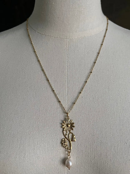 A historical jewelry inspired vintage style daisy flower pendant necklace with pearl dangle in gold toned stainless steel