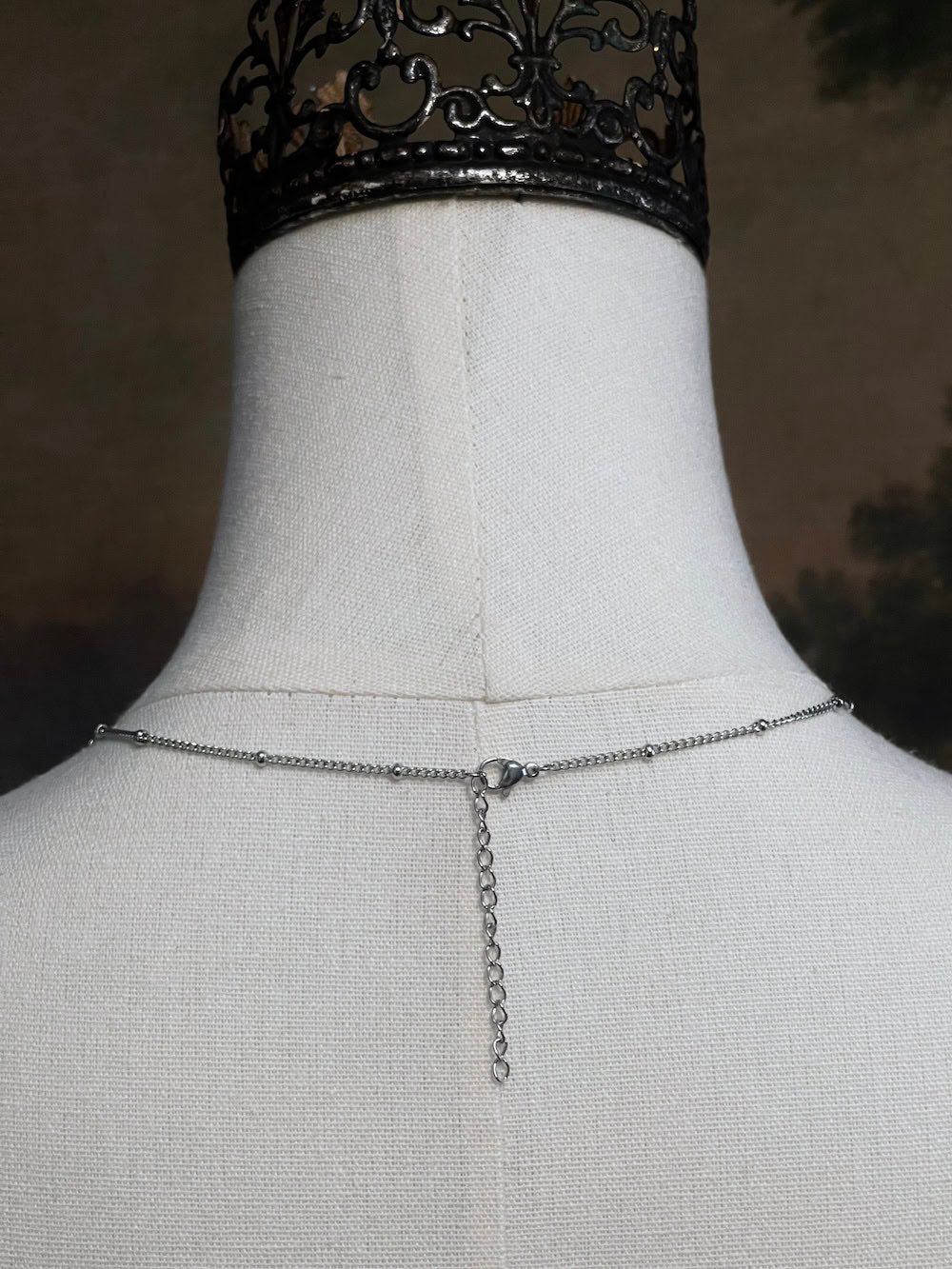 A mannequin wearing a historical jewelry inspired vintage style daisy flower pendant necklace with pearl dangle in silver toned stainless steel