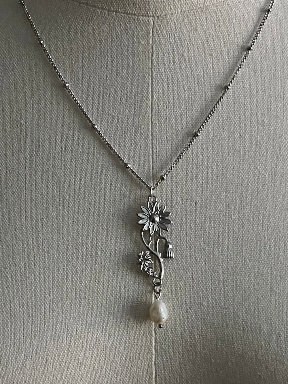 A mannequin wearing a historical jewelry inspired vintage style daisy flower pendant necklace with pearl dangle in silver toned stainless steel
