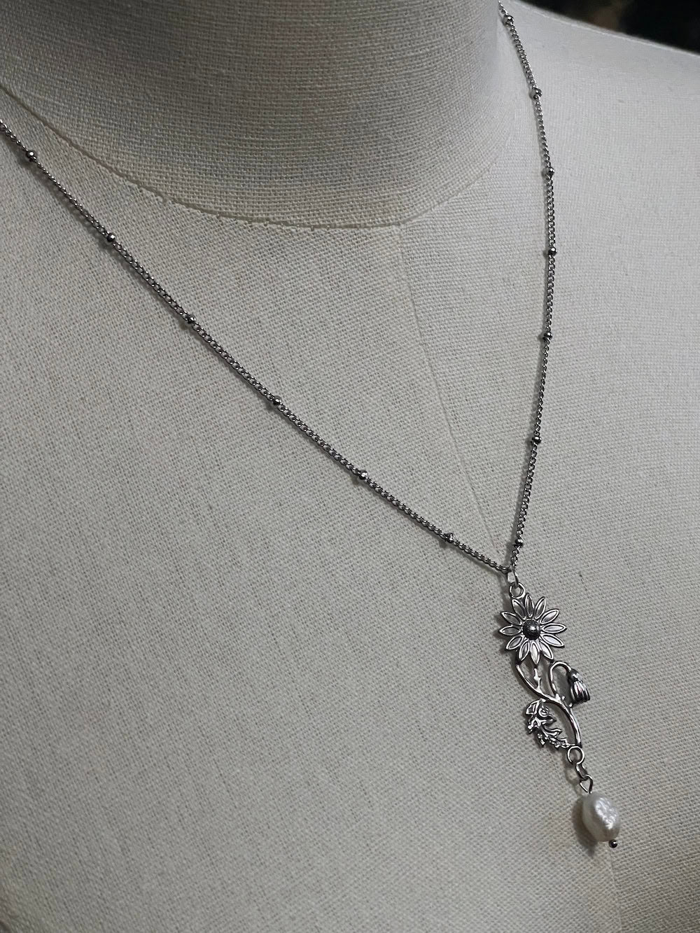 A mannequin wearing a historical jewelry inspired vintage style daisy flower pendant necklace with pearl dangle in silver toned stainless steel