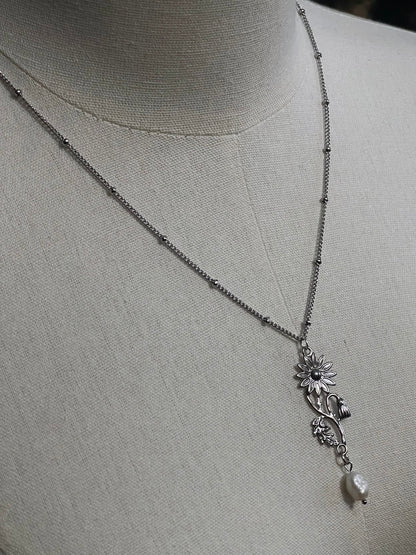 A mannequin wearing a historical jewelry inspired vintage style daisy flower pendant necklace with pearl dangle in silver toned stainless steel