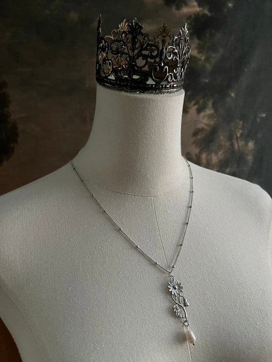 A mannequin wearing a historical jewelry inspired vintage style daisy flower pendant necklace with pearl dangle in silver toned stainless steel