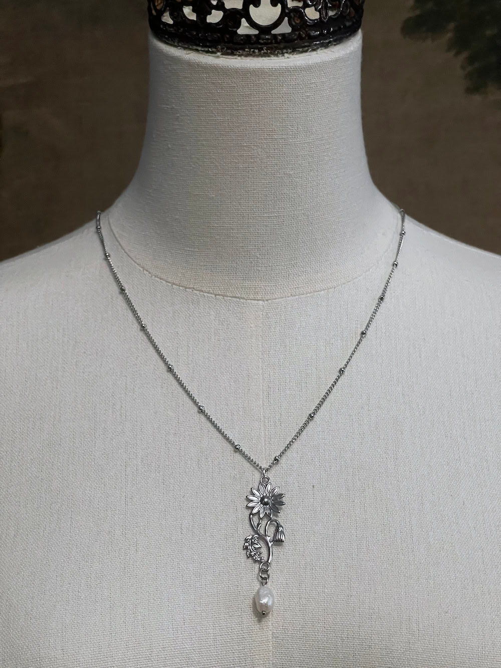 A mannequin wearing a historical jewelry inspired vintage style daisy flower pendant necklace with pearl dangle in silver toned stainless steel