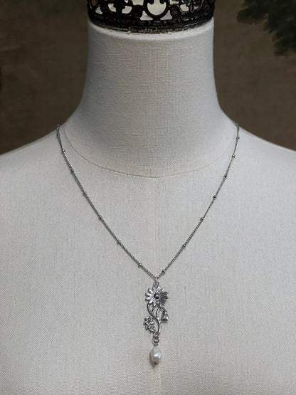 A mannequin wearing a historical jewelry inspired vintage style daisy flower pendant necklace with pearl dangle in silver toned stainless steel