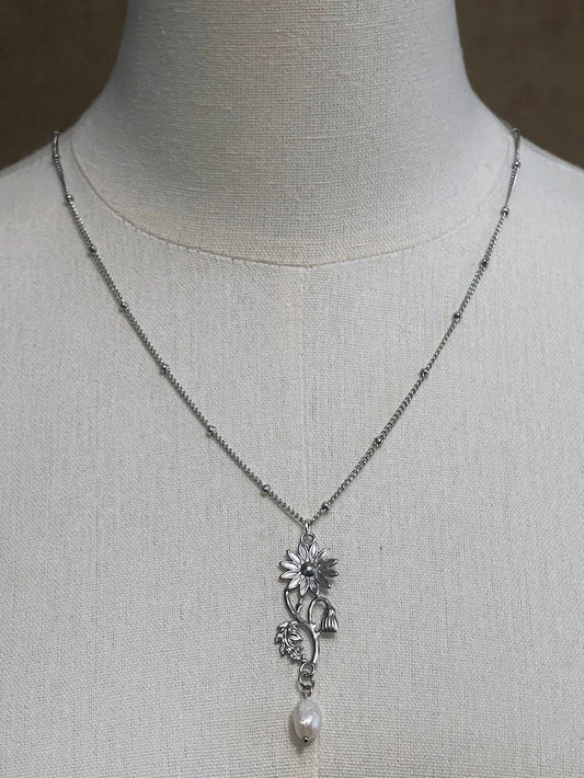 A mannequin wearing a historical jewelry inspired vintage style daisy flower pendant necklace with pearl dangle in silver toned stainless steel