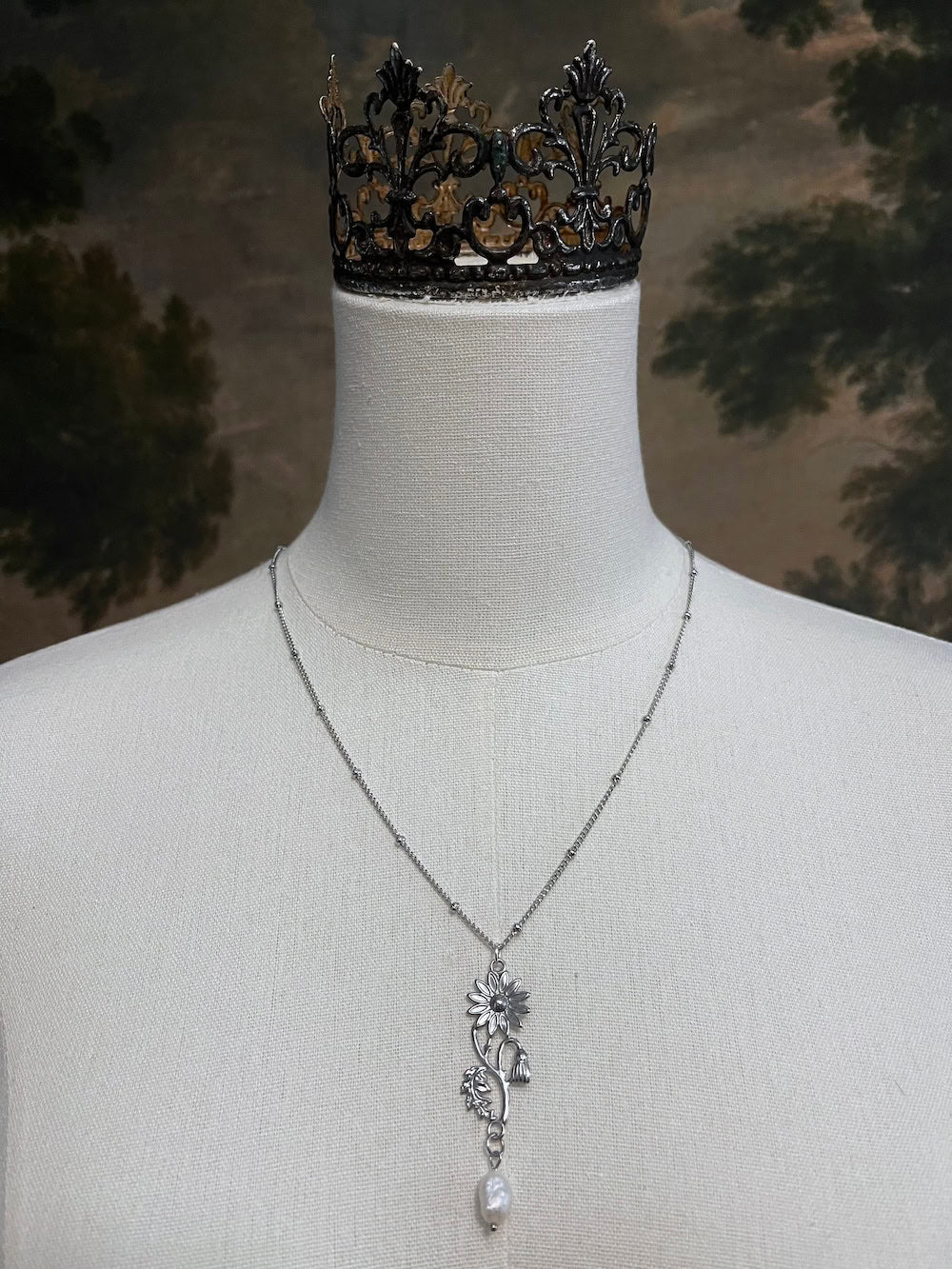 A mannequin wearing a historical jewelry inspired vintage style daisy flower pendant necklace with pearl dangle in silver toned stainless steel