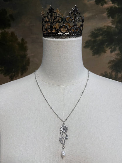 A mannequin wearing a historical jewelry inspired vintage style daisy flower pendant necklace with pearl dangle in silver toned stainless steel