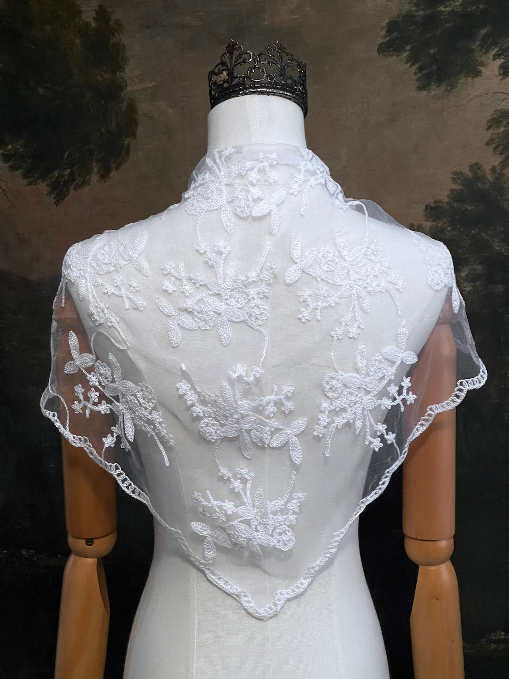 Mannequin wearing a vintage style white lace headscarf babushka triangle headdress made from floral embroidery lace as a shawl against an art history background