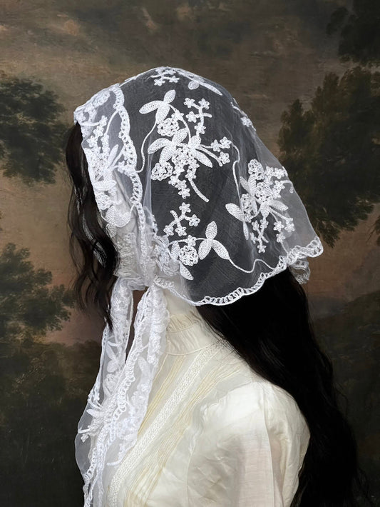 Mannequin wearing a vintage style white lace headscarf babushka triangle headdress made from floral embroidery lace against an art history background