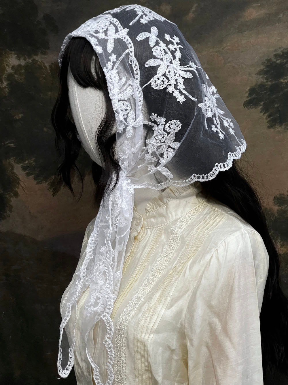 Mannequin wearing a vintage style white lace headscarf babushka triangle headdress made from floral embroidery lace against an art history background
