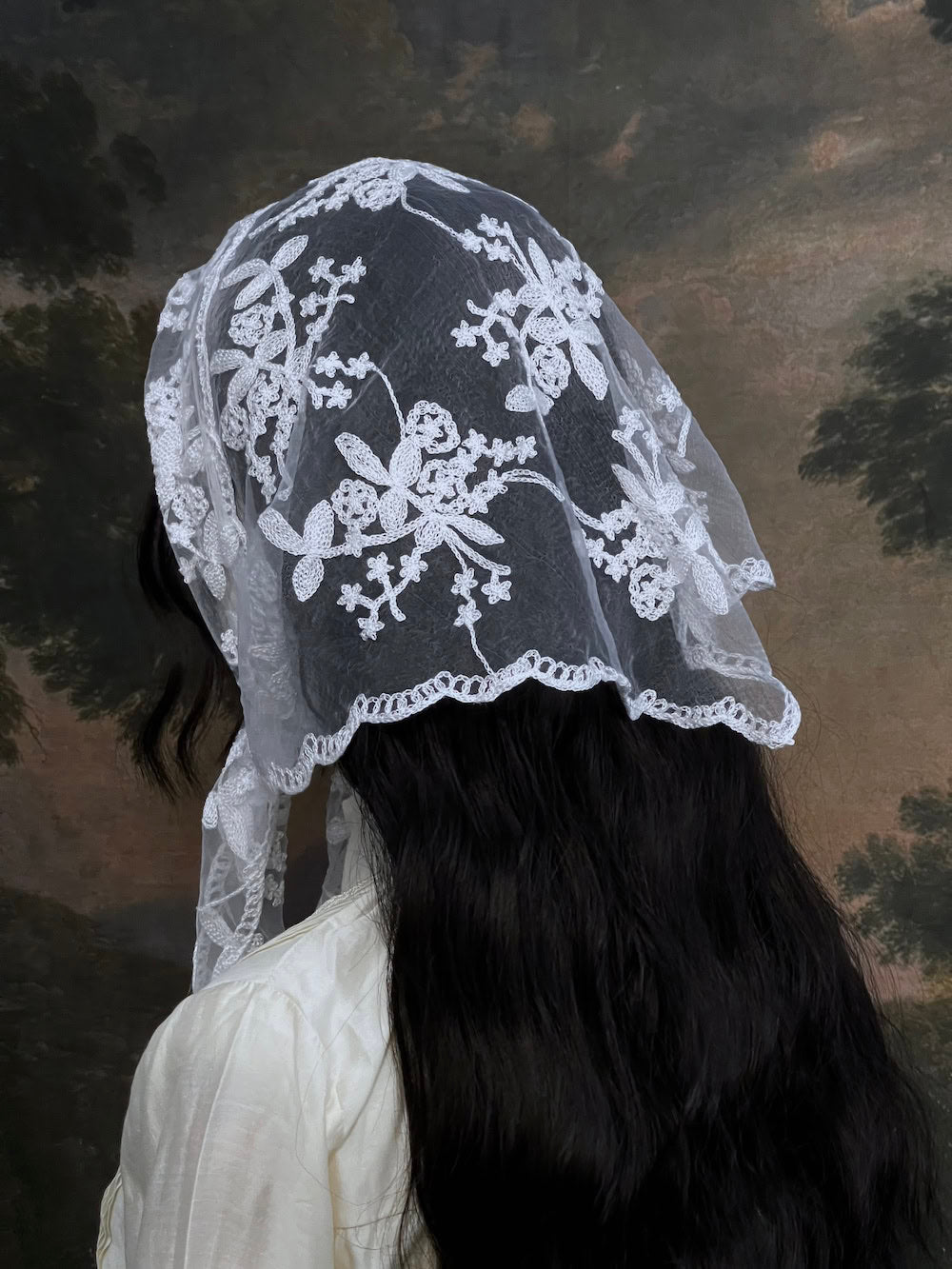 Mannequin wearing a vintage style white lace headscarf babushka triangle headdress made from floral embroidery lace against an art history background