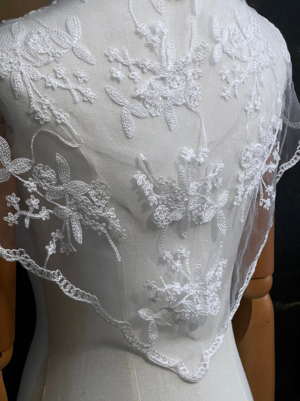Mannequin wearing a vintage style white lace headscarf babushka triangle headdress made from floral embroidery lace as a shawl against an art history background